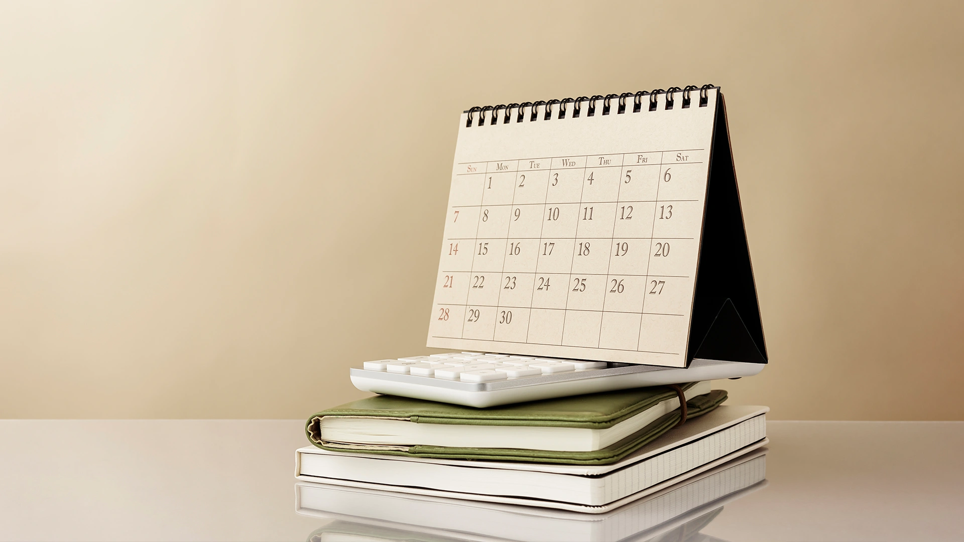 Calendário de mesa sobre calculadora e cadernos de anotações