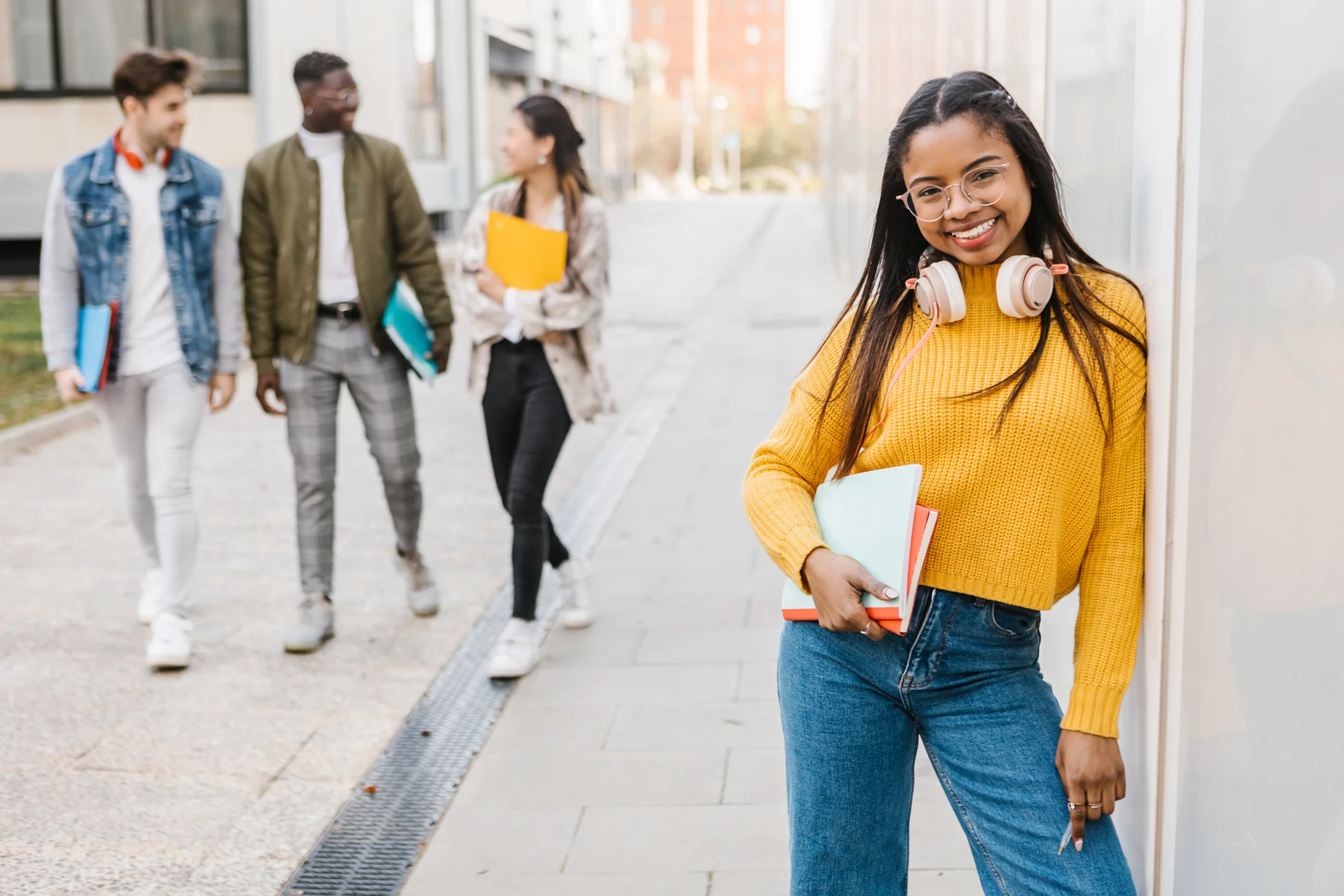 Estudante jovem sorridente com livros e fones de ouvido no campus universitário