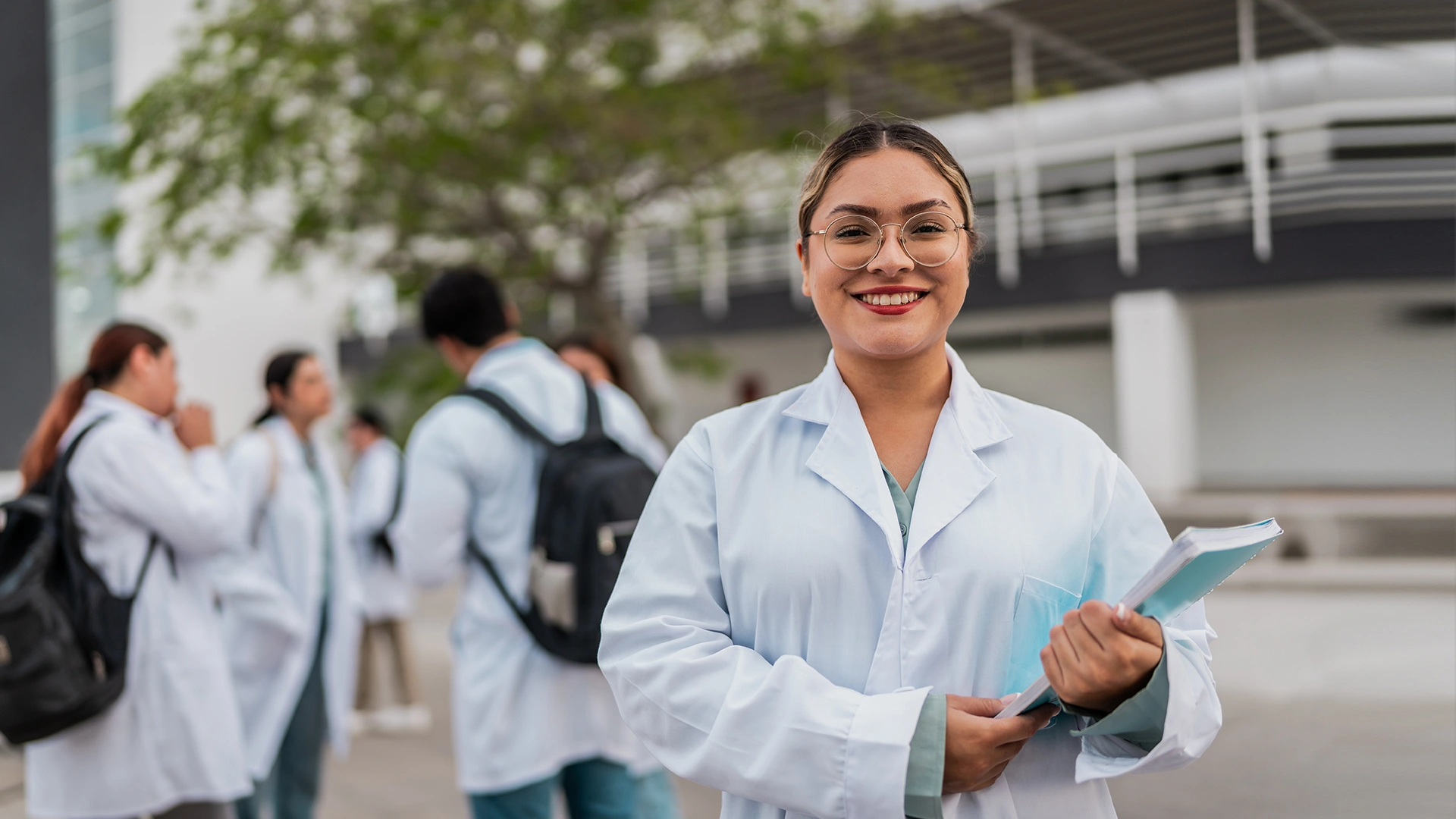 Estudante de medicina sorridente com jaleco branco segurando cadernos no campus