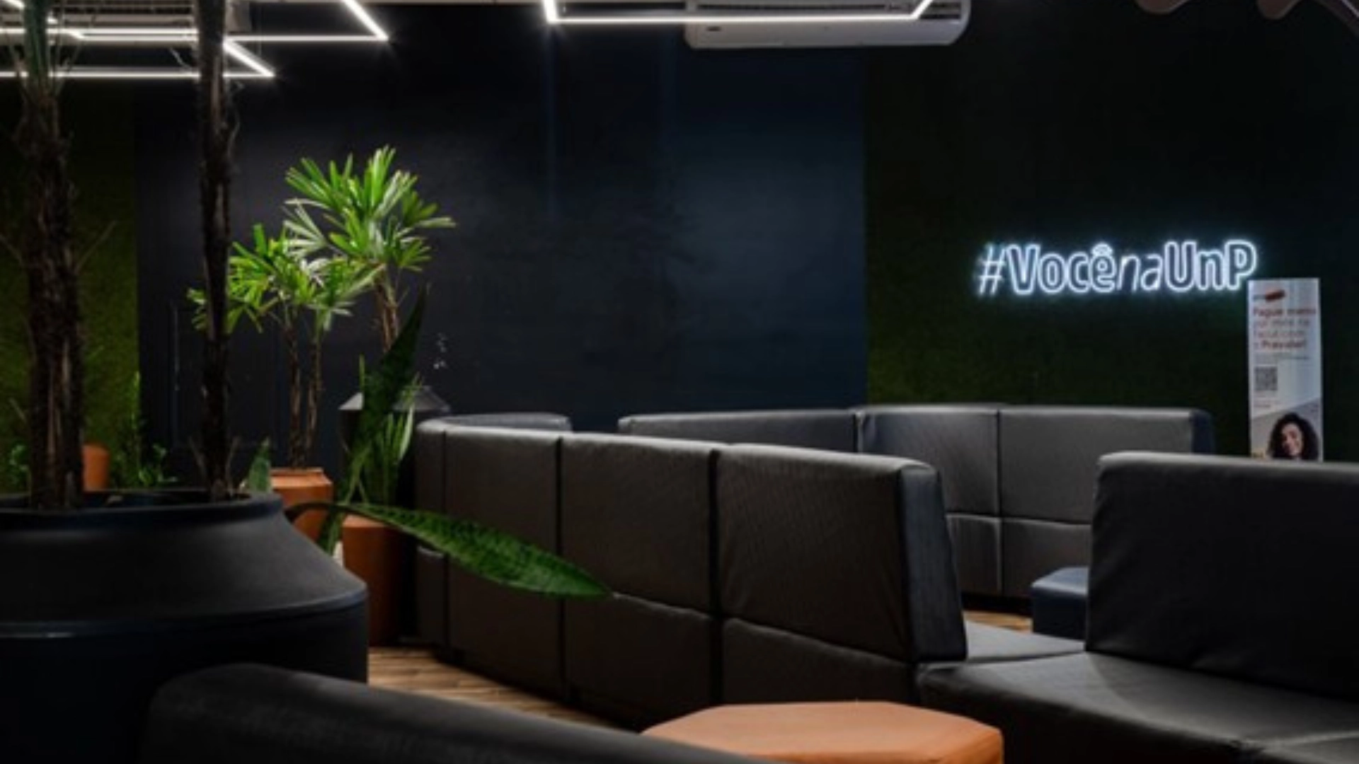 Espaço de convivência moderno da UnP com sofás pretos e decoração em neon #VocênaUnP