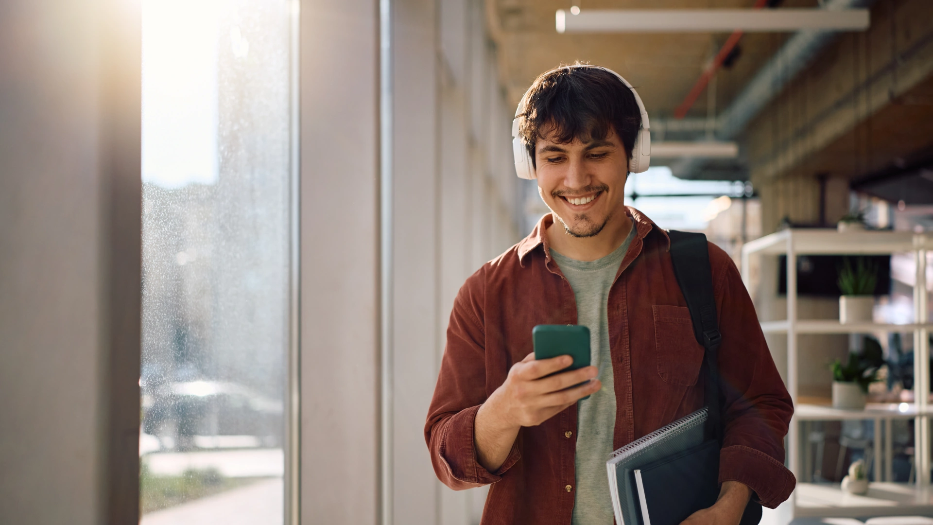Estudante universitário sorrindo enquanto usa smartphone e fones de ouvido no campus