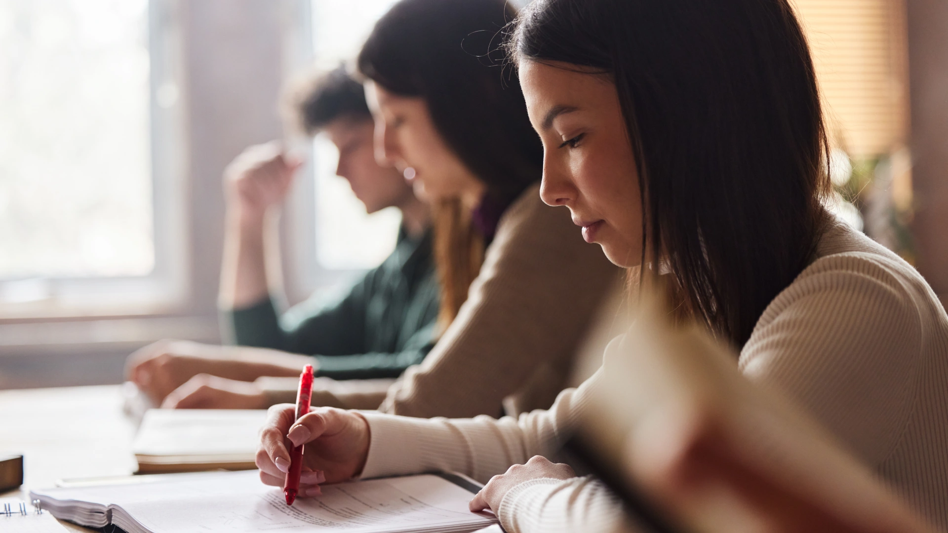 Alunos universitários focados em seus estudos e anotações em uma sala de aula iluminada pela luz natural