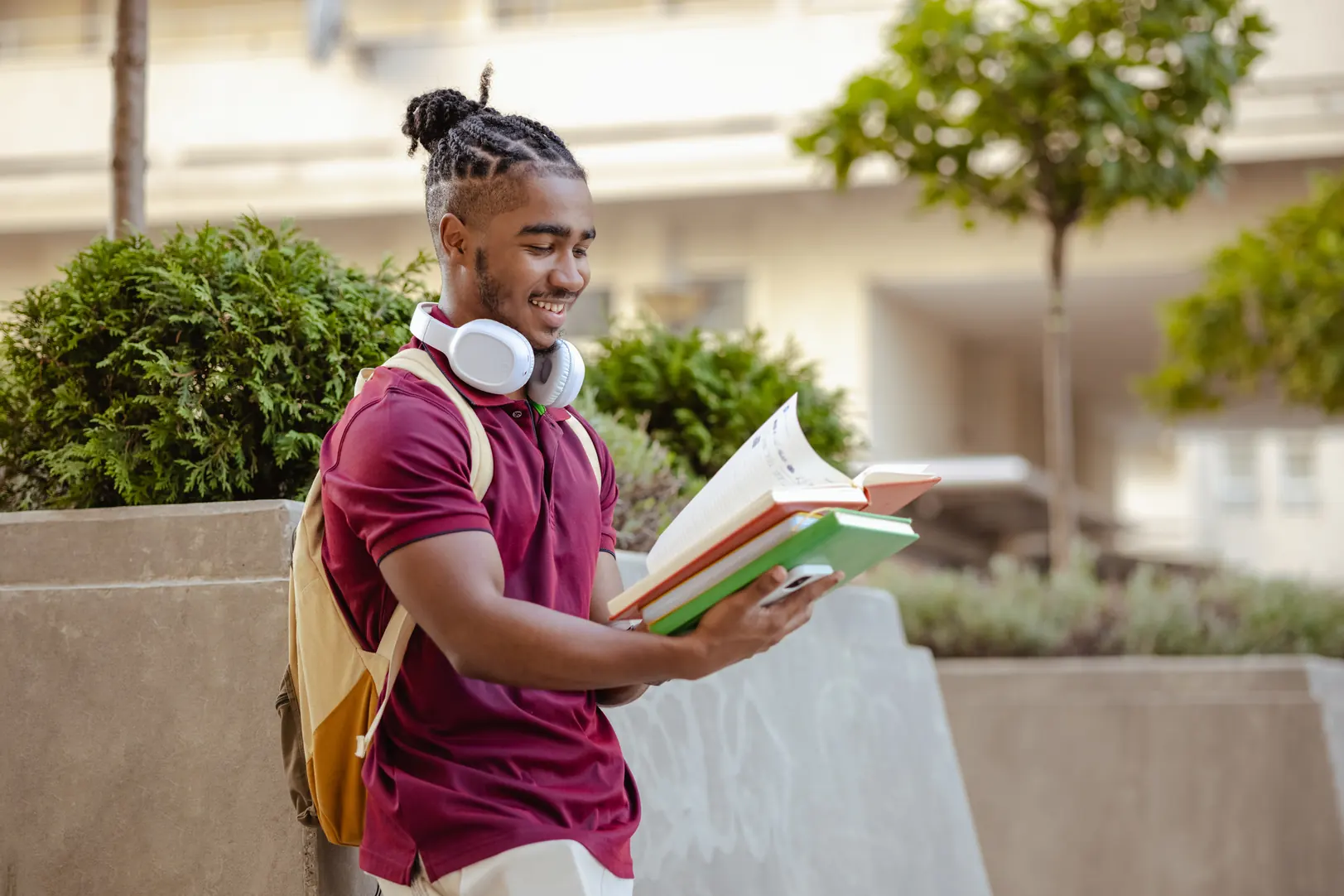 Estudante universitário negro sorrindo enquanto lê livros em um campus ao ar livre