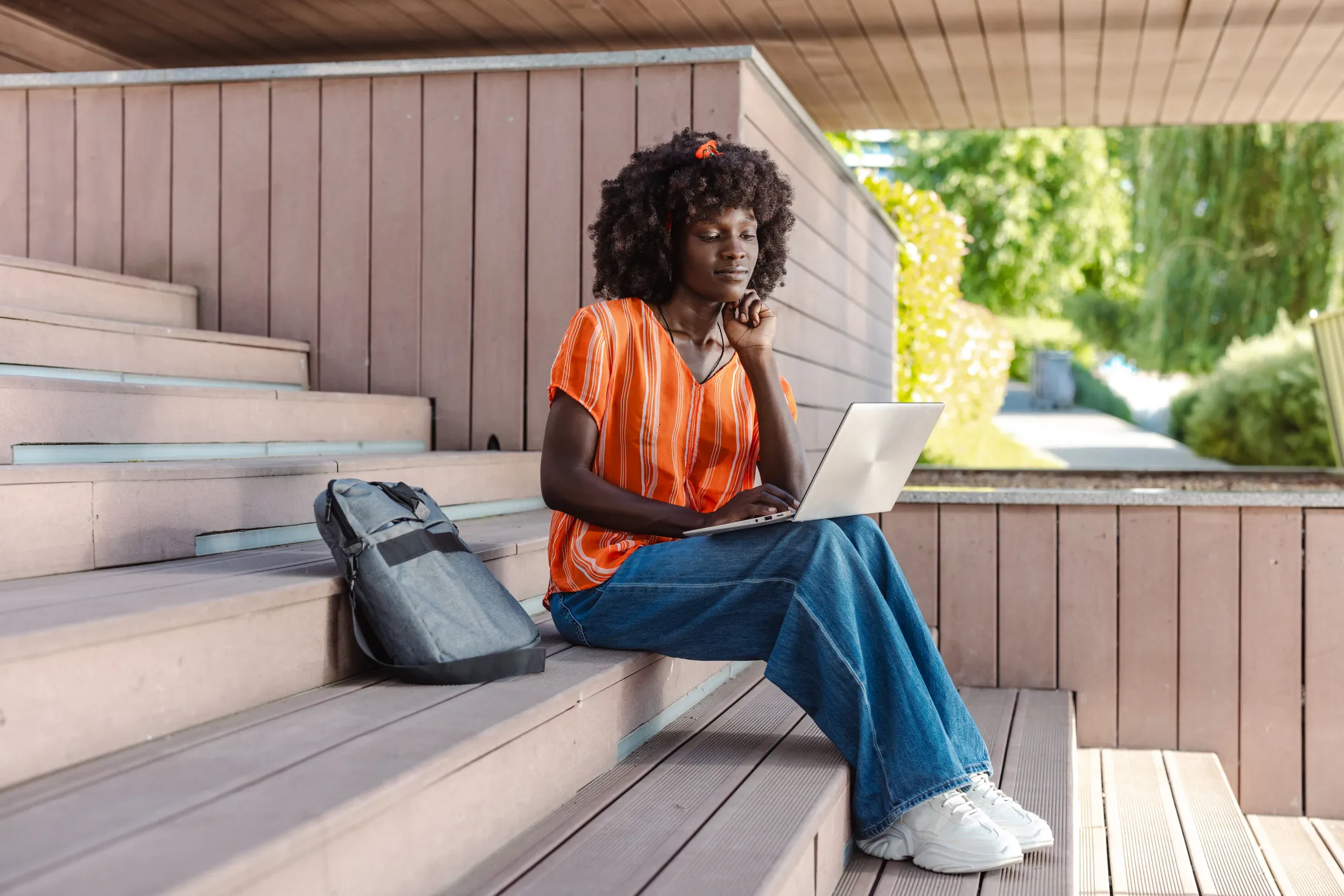 Estudante negra sentada em uma escadaria de madeira usando um laptop ao ar livre
