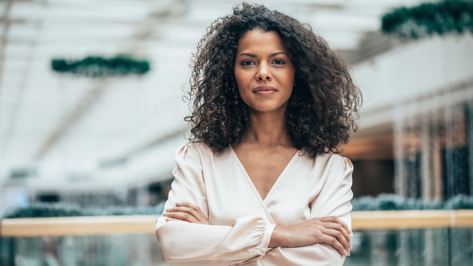 Mulher jovem com cabelos cacheados cruzando os braços em um ambiente corporativo