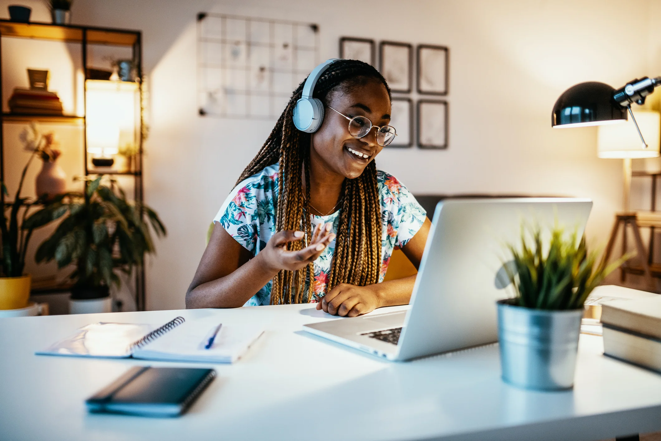 Estudante jovem sorridente participando de aula online via notebook com fones de ouvido em um ambiente de estudo aconchegante