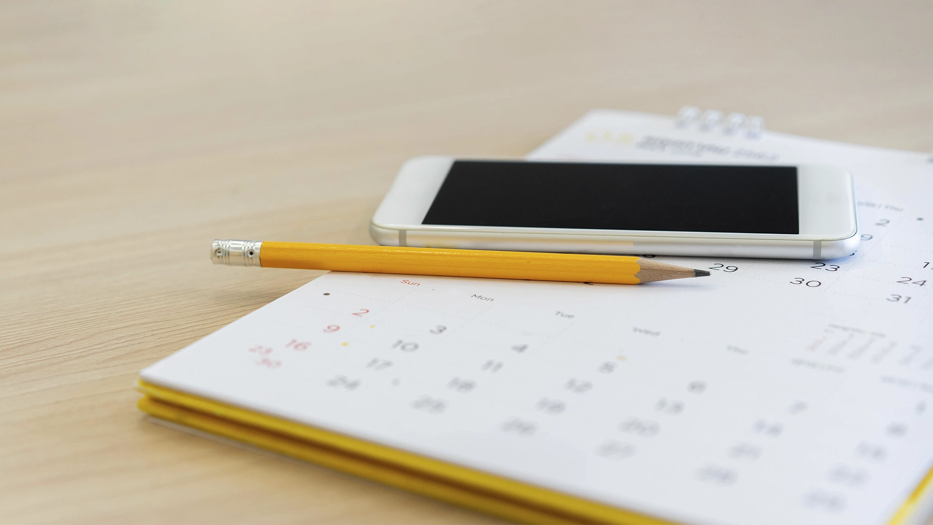 Smartphone e lápis sobre calendário de mesa em fundo de madeira