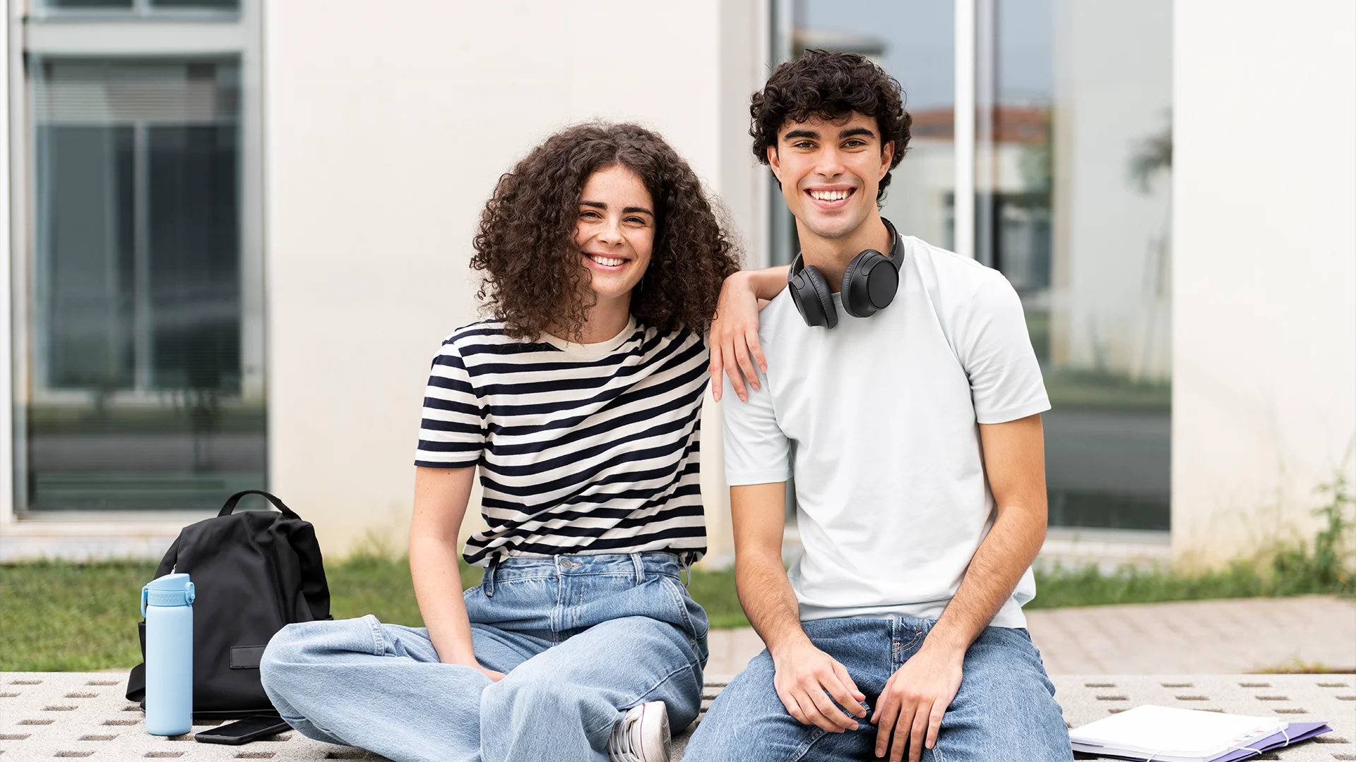 Estudantes universitários sorridentes sentados no campus com mochilas e cadernos