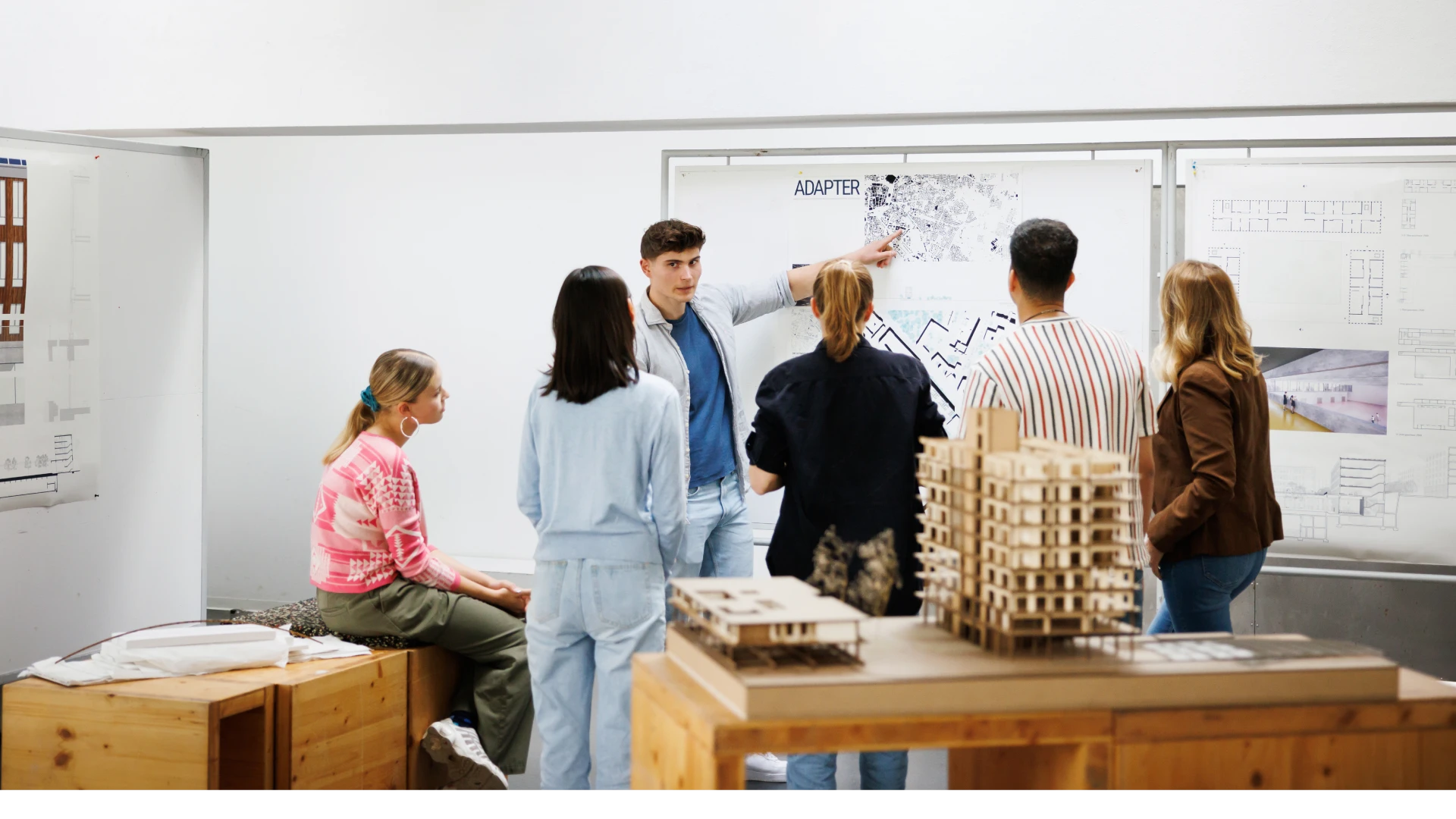Alunos de arquitetura colaborando em um projeto acadêmico com maquetes e plantas em um ambiente de estúdio