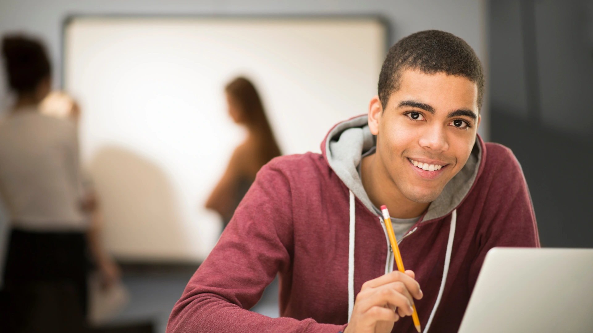 Aluno sorrindo e sentado segurando um lápis na extensão e fazendo seu curso de extensão