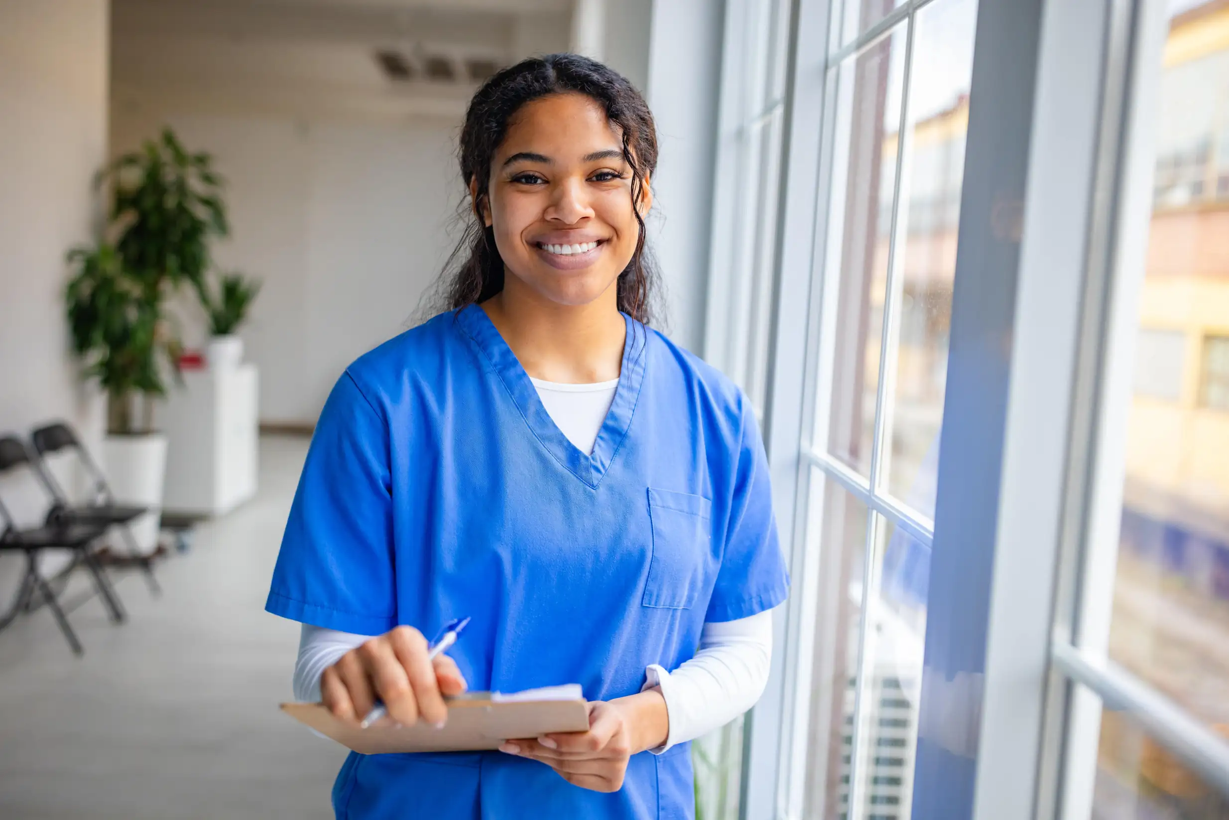 Estudante de enfermagem sorridente usando uniforme azul com prancheta em hospital