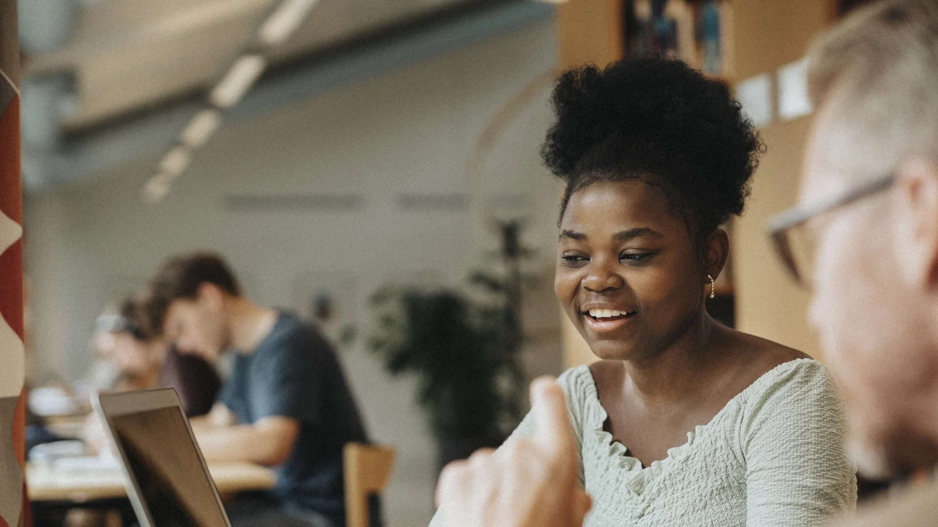 Estudante negra sorridente conversando com colega em ambiente de estudo colaborativo