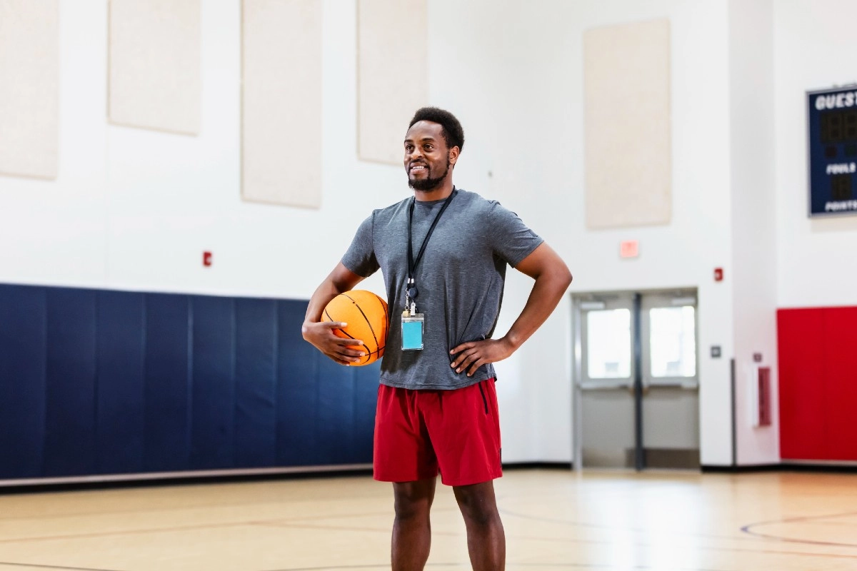 Professor de Educação Física segurando uma bola de basquete em uma quadra esportiva