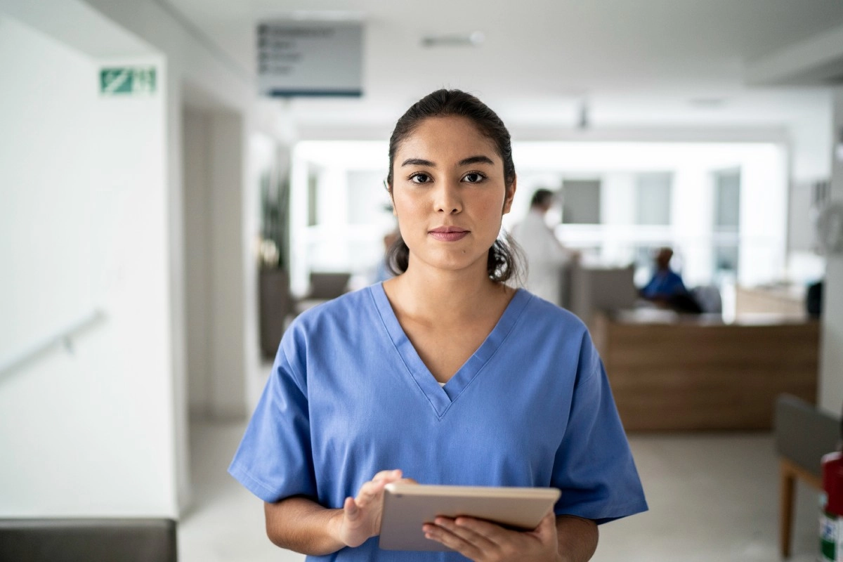 Profissional de biomedicina vestindo uniforme azul segurando um tablet em ambiente hospitalar