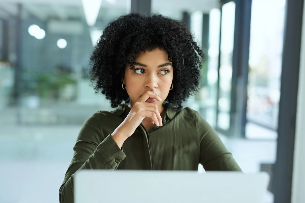 Mulher pensativa olhando para o computador enquanto decide entre pós-graduação ou MBA