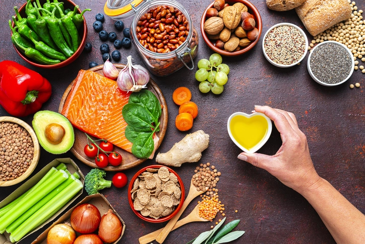 Variedade de alimentos saudáveis sobre uma mesa, incluindo peixe, vegetais, grãos, sementes e azeite