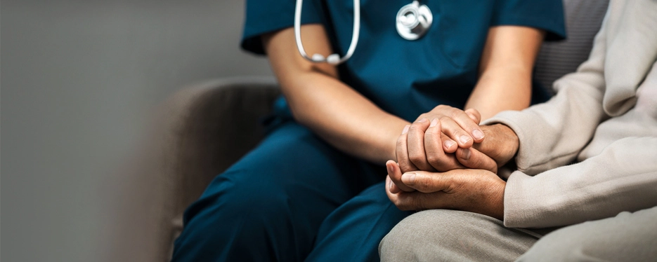 Curso de Biomedicina: a importância da humanização no atendimento clínico e no cuidado com o paciente Profissional de saúde segurando a mão de um paciente idoso em sinal de acolhimento e cuidado