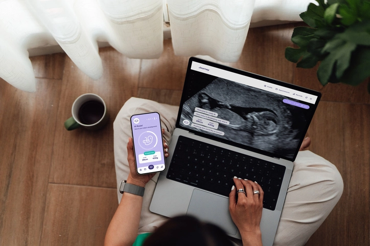 Mulher utilizando smartphone e laptop para acompanhar o desenvolvimento do feto através de um aplicativo de gravidez