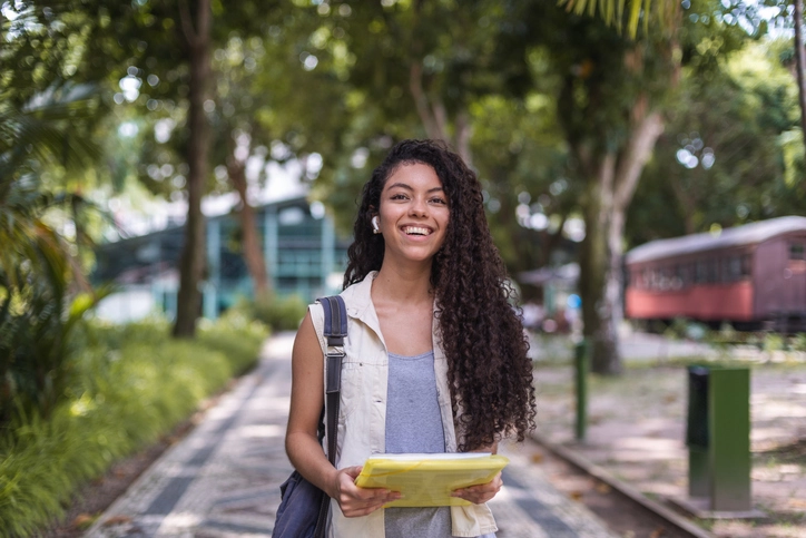 Estudante universitária sorridente caminhando pelo campus do IBMR segurando materiais de aula