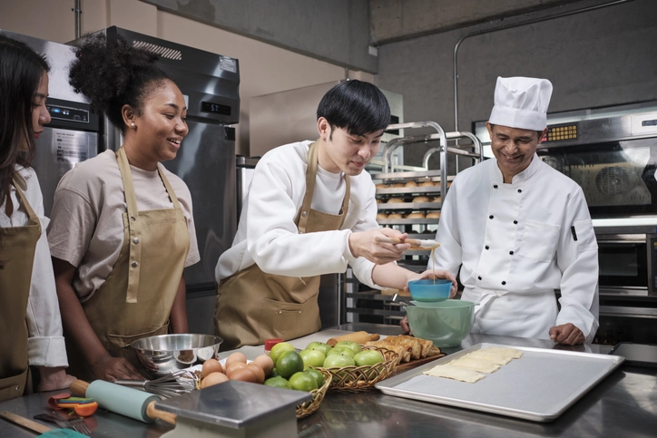 Estudantes de gastronomia em aula prática com chef de cozinha em ambiente profissional