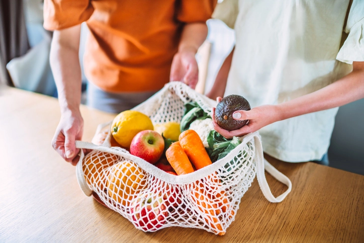 Pessoas organizando uma sacola de compras com alimentos saudáveis e frescos para promover um estilo de vida sustentável Pessoas segurando uma sacola reutilizável cheia de frutas e vegetais frescos
