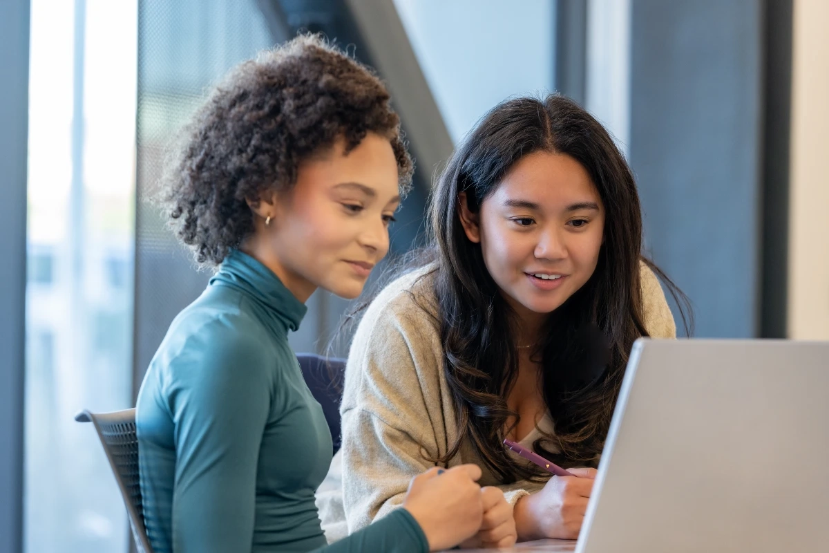Duas estudantes universitárias analisando informações em um notebook para transferência de curso