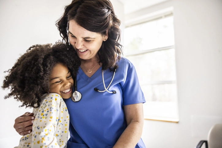 Enfermeira sorridente abraçando uma criança paciente em um ambiente hospitalar