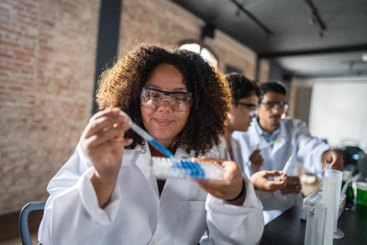 Estudante de biomedicina com jaleco e óculos de proteção realizando experimento em laboratório