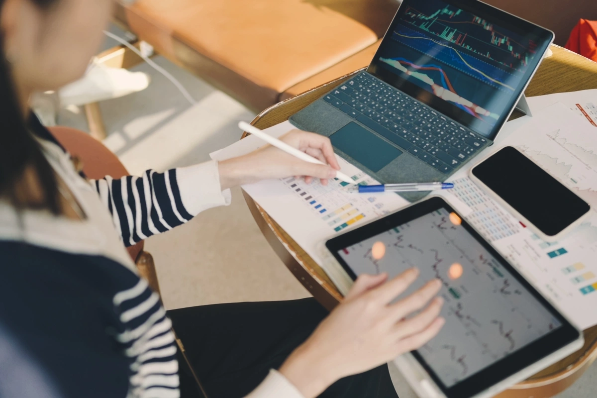 Estudante de Ciências Contábeis analisando gráficos financeiros em um tablet e notebook