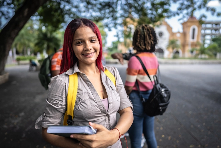 Estudante sorridente com mochila e caderno em um campus universitário