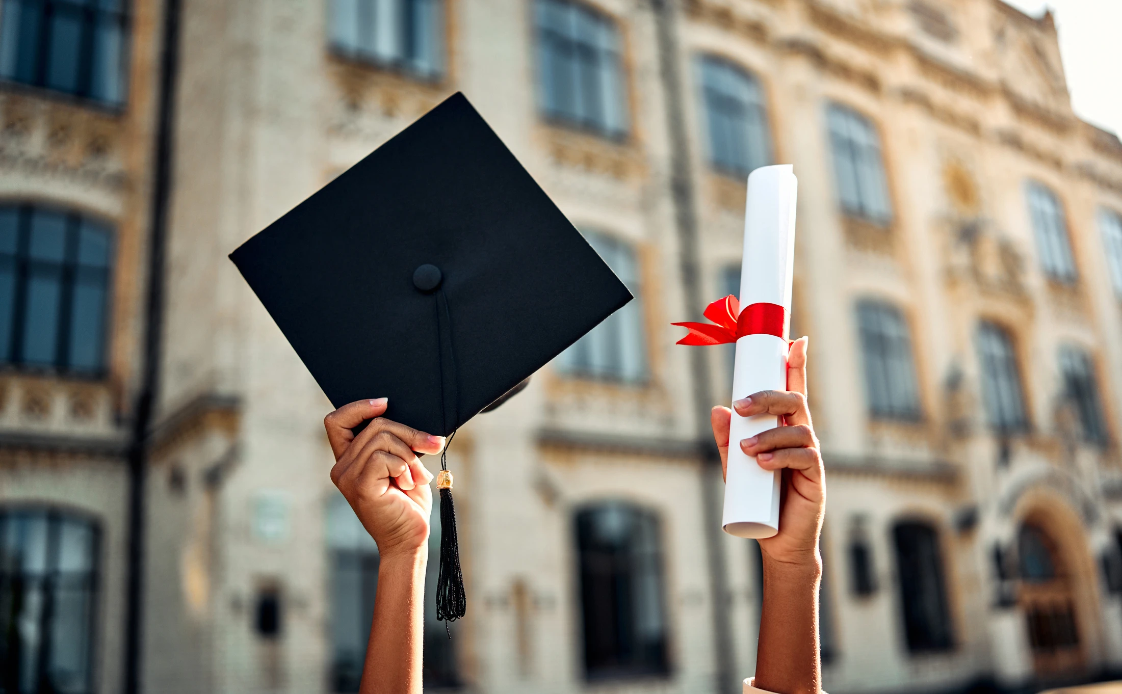 Estudante celebrando a formatura com capelo e diploma em frente a prédio universitário histórico