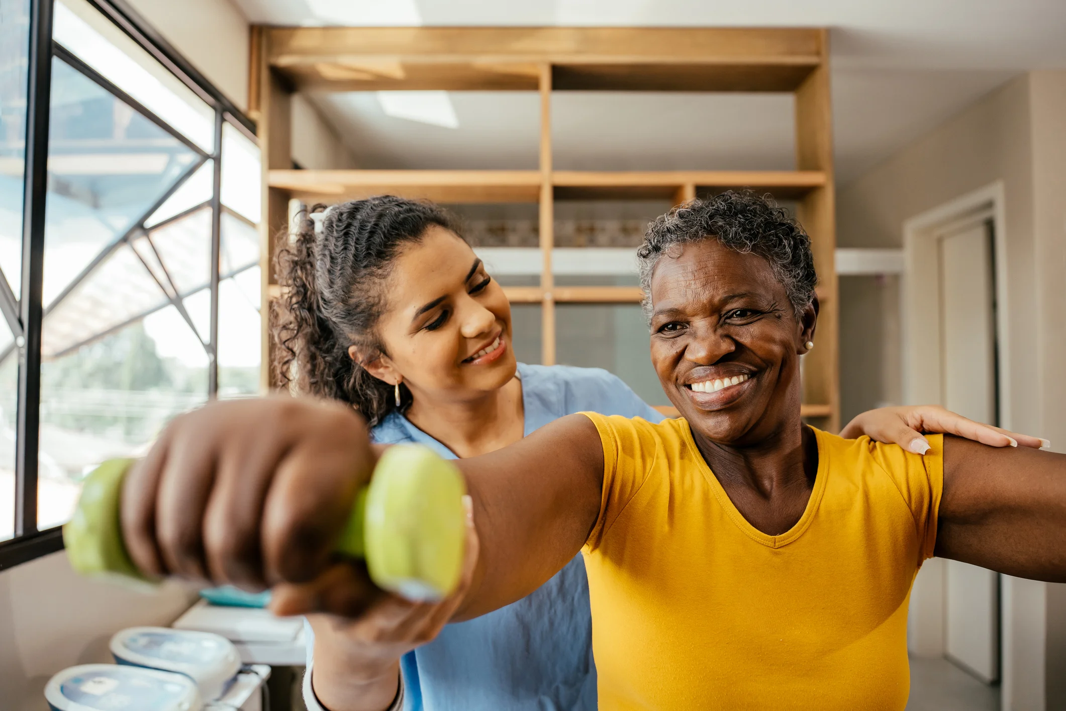 Fisioterapeuta auxiliando idosa em exercícios com halteres Fisioterapeuta acompanhando idosa durante sessão de reabilitação física com halteres para fortalecimento muscular