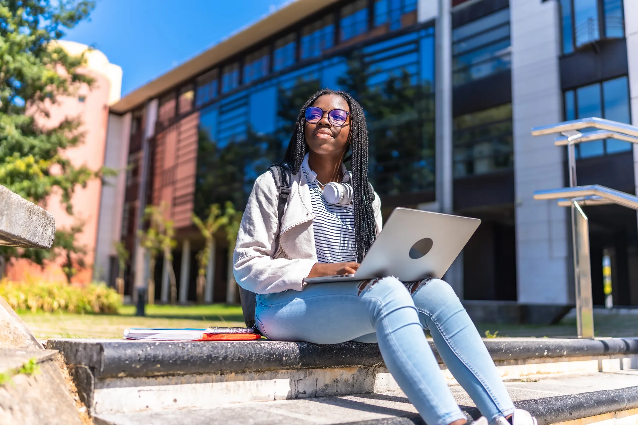 Estudante universitária negra sentada nos degraus do campus da universidade estudando com seu laptop em um dia ensolarado
