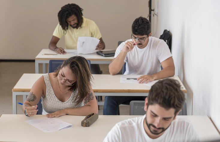 Alunos universitários focados em uma avaliação acadêmica em ambiente de sala de aula Estudantes concentrados realizando prova em sala de aula universitária