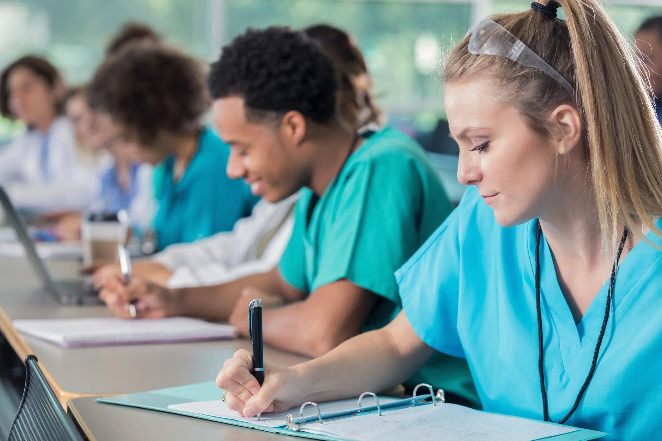 Estudantes de biomedicina concentrados escrevendo em cadernos durante aula prática