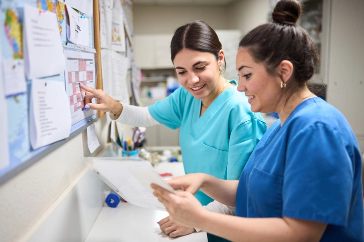 Enfermeiras colaborando e revisando escalas de atendimento em ambiente hospitalar para otimização do fluxo de trabalho Duas enfermeiras sorridentes analisando um cronograma de trabalho em um hospital