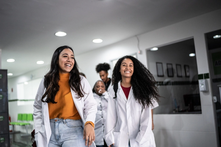Estudantes universitárias da área da saúde caminhando e sorrindo em corredor de faculdade