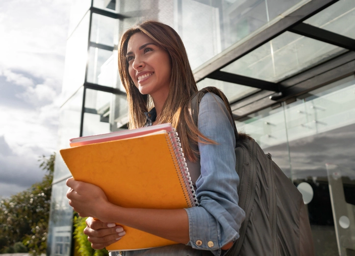 Estudante universitária sorridente segurando cadernos e mochila no campus