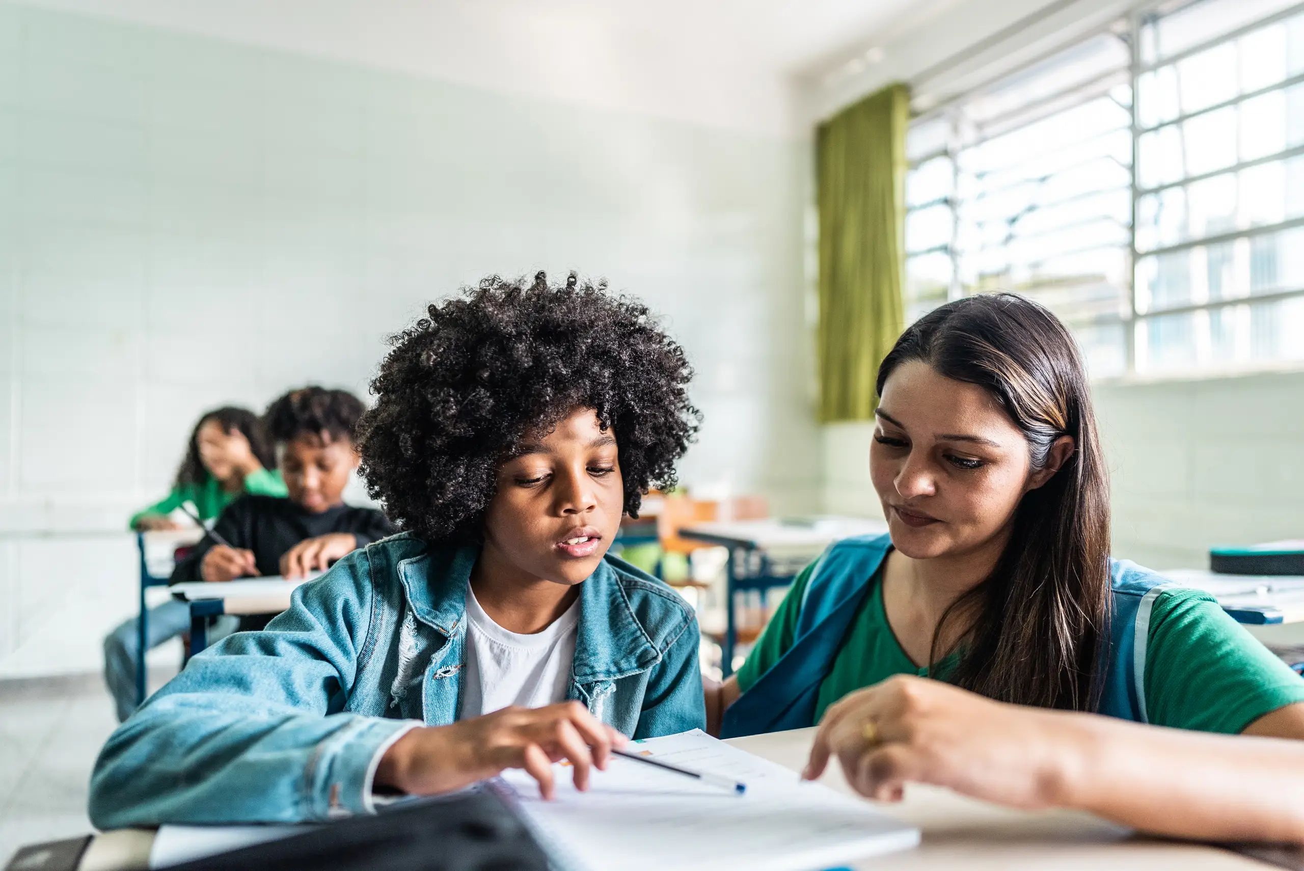 Professora auxiliando aluno em sala de aula durante curso de pedagogia
