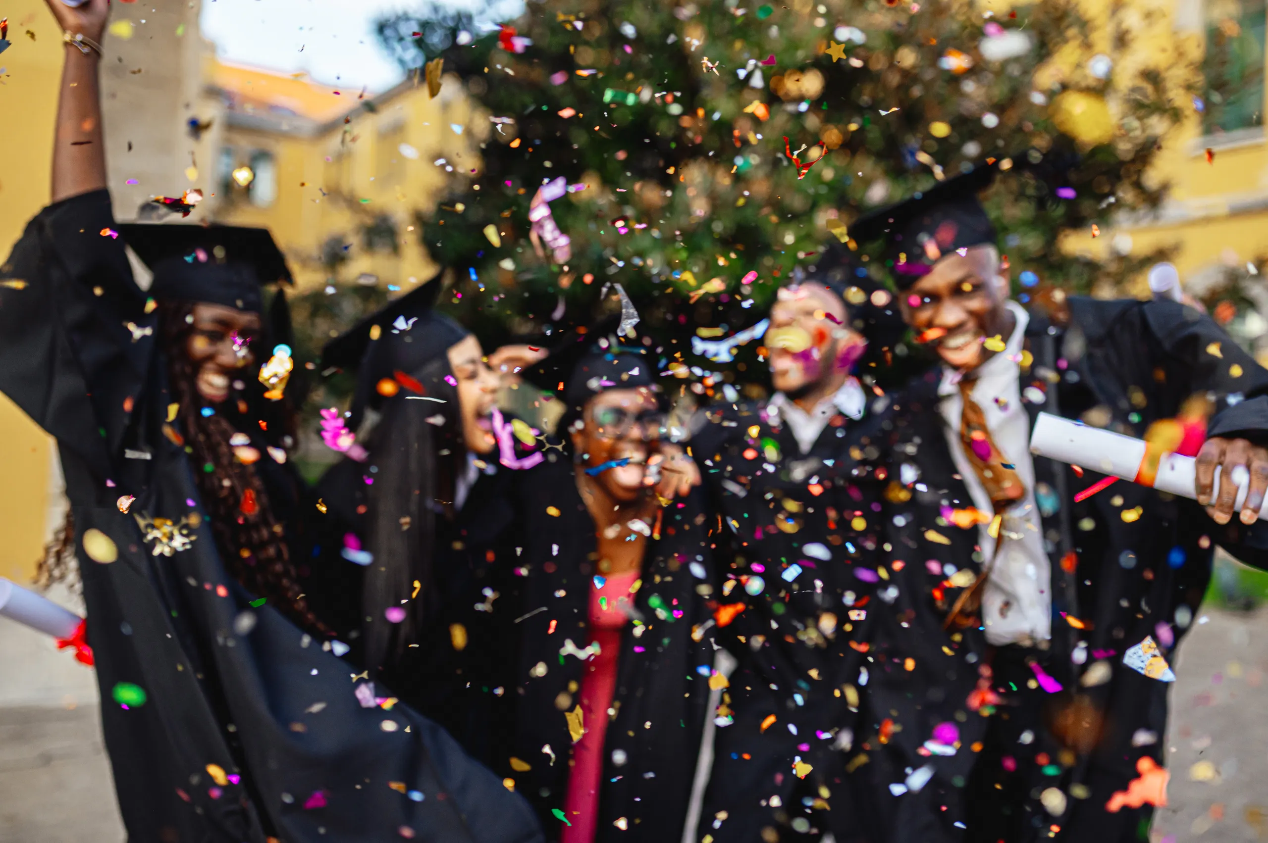 Grupo de estudantes universitários celebrando a formatura com becas e confetes