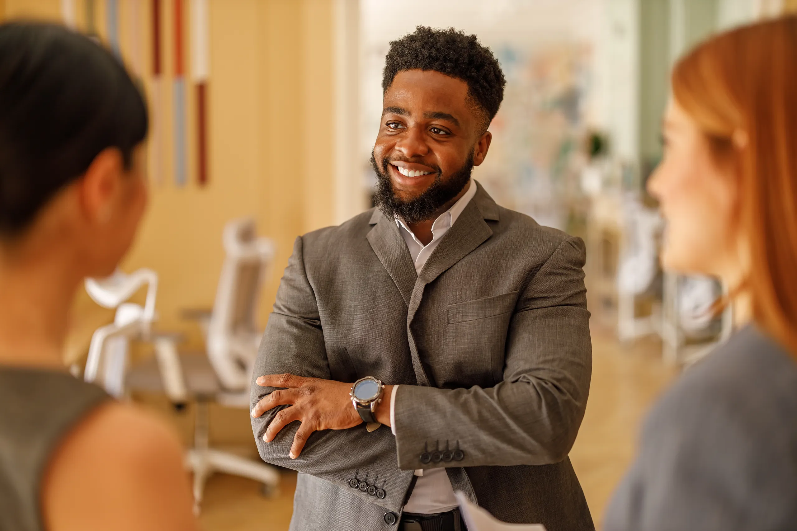 Homem negro sorrindo de terno conversando com colegas em um ambiente de escritório profissional