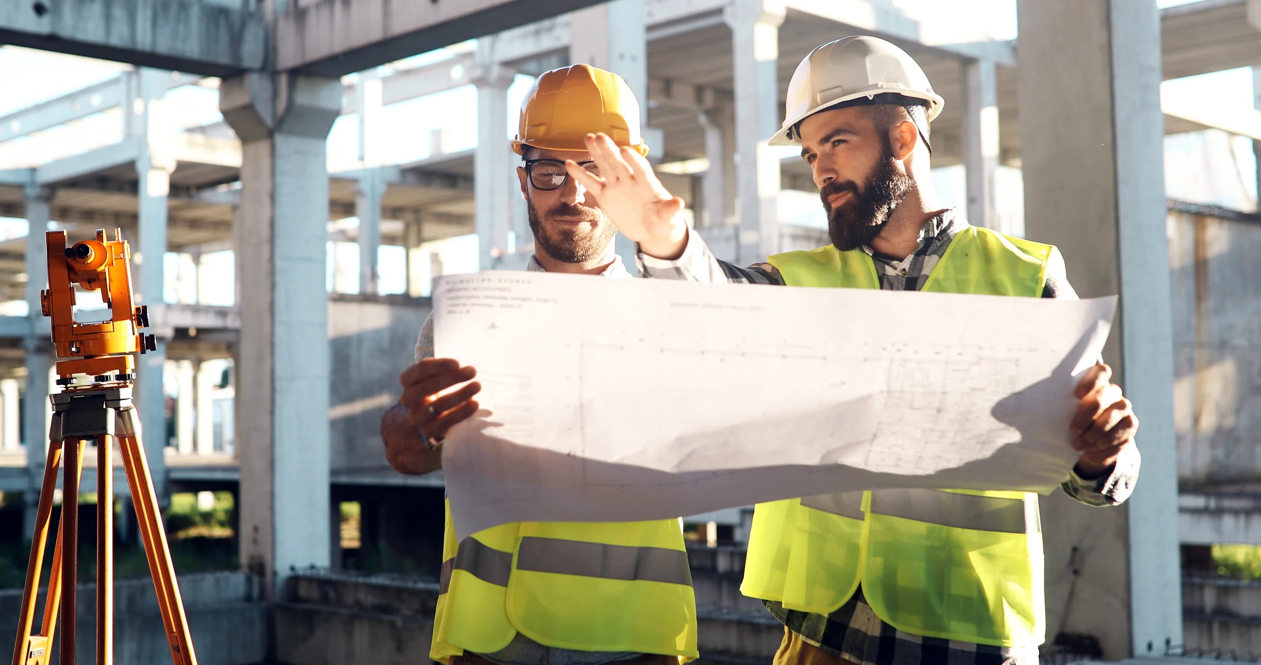 Dois engenheiros de capacete analisando uma planta de construção em um canteiro de obras.
