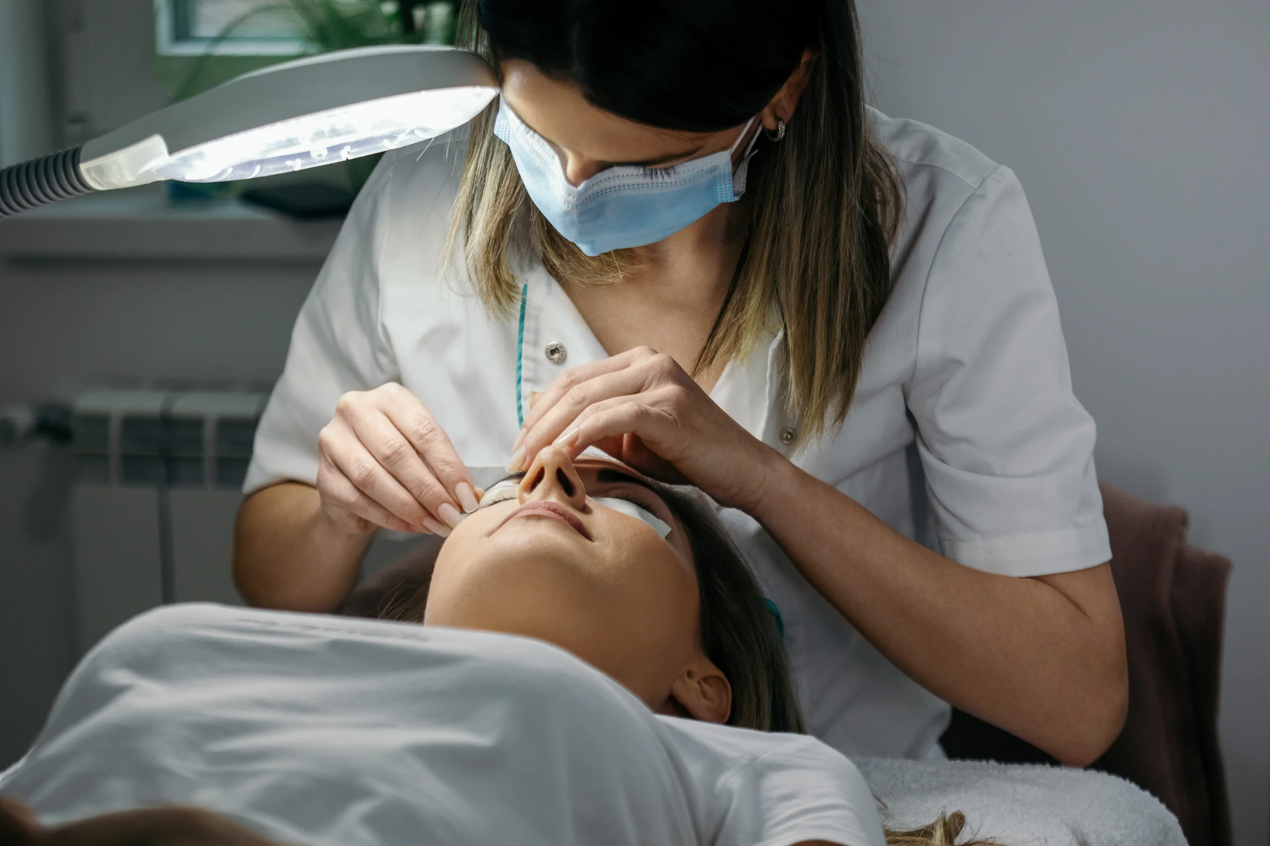 Esteticista aplicando procedimento de extensão de cílios em uma cliente em uma clínica de estética