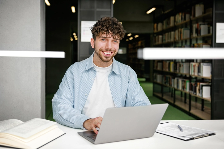 Estudante universitário focado estudando em uma biblioteca acadêmica com laptop e livros para pesquisa