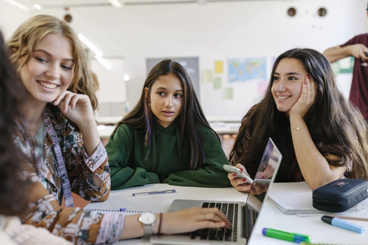 Grupo de estudantes universitárias estudando juntas com notebook em sala de aula moderna