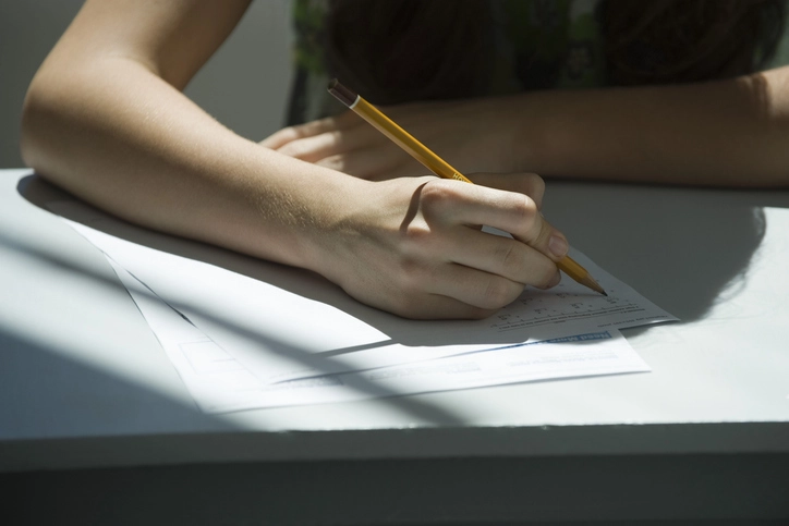 Estudante preenchendo prova ou formulário com lápis em uma mesa iluminada