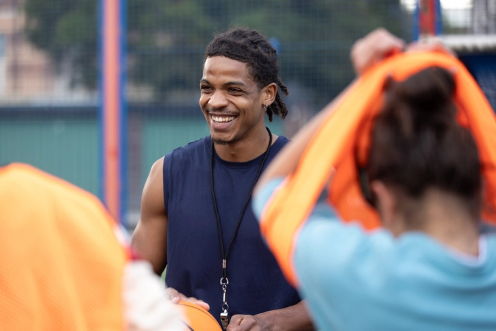 https://estaticos.animaeducacao.com.br/medias/20251215174306/GettyImages-2239717939.webp Treinador de basquete sorridente instruindo atletas em uma quadra esportiva