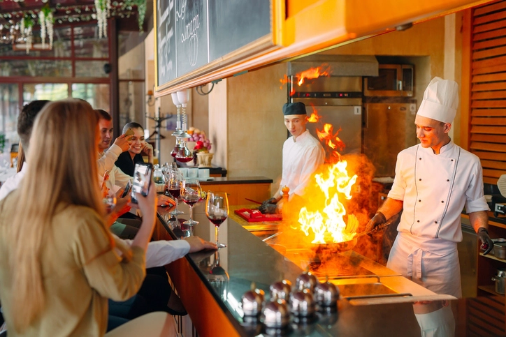 Chef cozinhando com fogo em restaurante para clientes que observam e tiram fotos