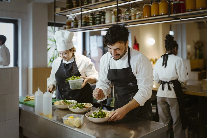 Equipe de chefs profissionais preparando saladas frescas em uma cozinha de restaurante comercial.