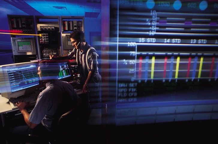 Técnicos monitorando dados e sistemas em uma sala de controle industrial com computadores